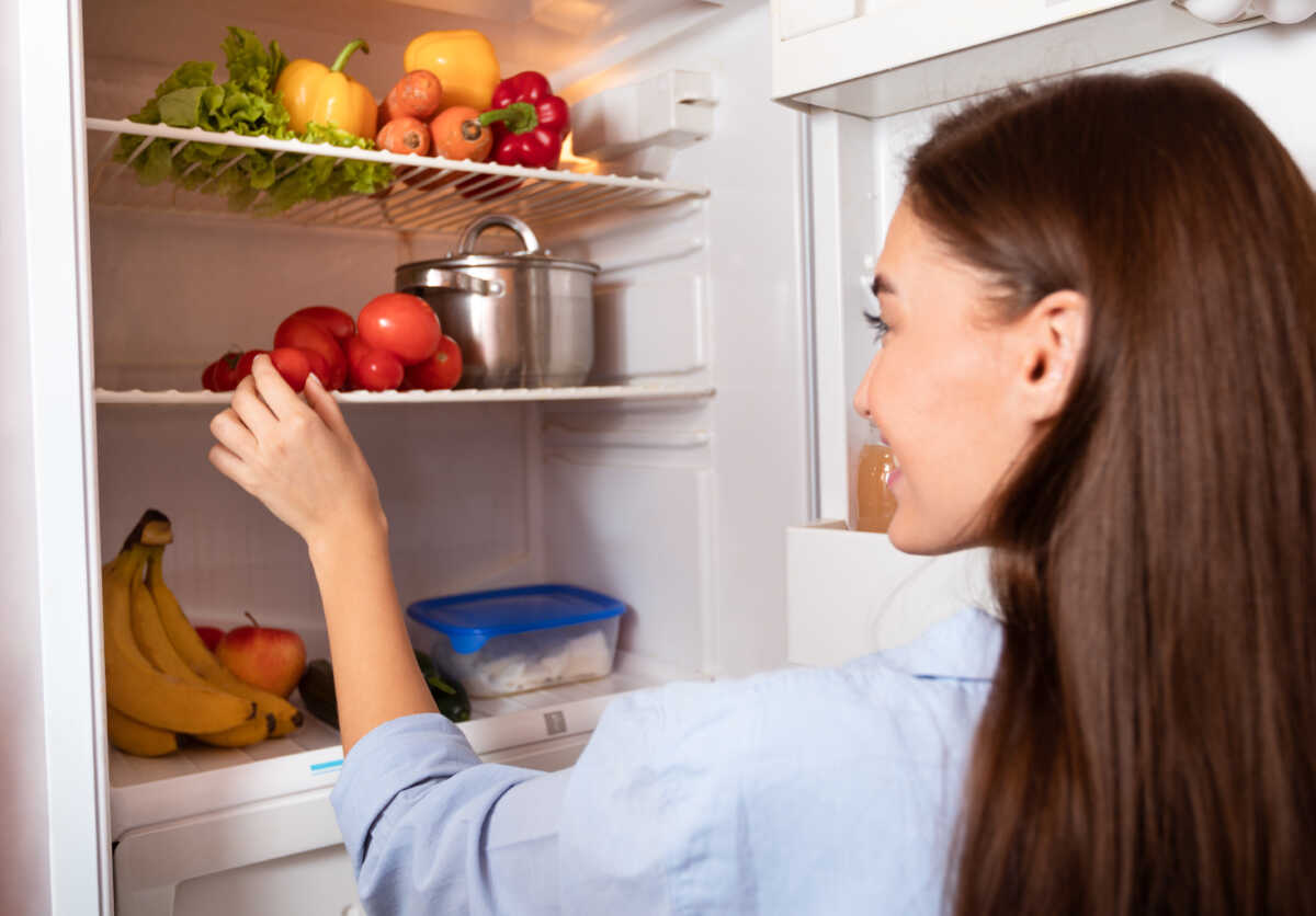 Young housewife taking organic vegetables from fridge at home, free space