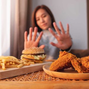 A woman making hand sign to refuse a hamburger, french fries and fried chicken on the table for dieting and healthy eating concept