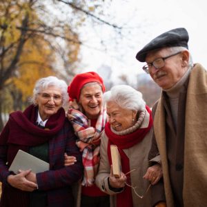 A group of happy senior friends with books on walk outdoors in park in autumn, talking and laughing