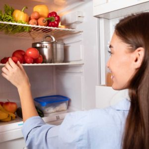 Young housewife taking organic vegetables from fridge at home, free space